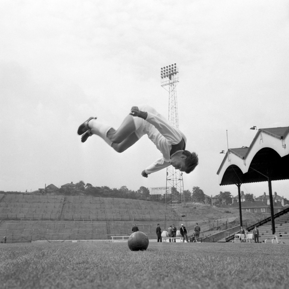 برایان کینسی بازیکن تیم چارلتون - Charlton’s Brian Kinsey somersaults over a football as he limbers up at The Addick’s pre-season training session at The Valley, 1965