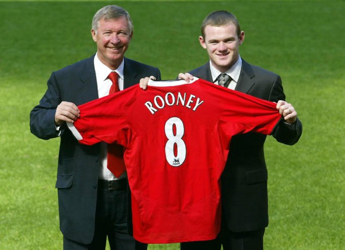 Ferguson helps hold Wayne Rooney’s new work clothes aloft following the latter’s £25+ million transfer from Everton, September 2004